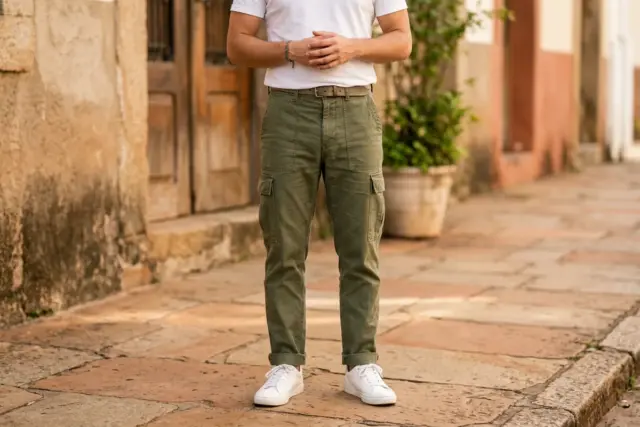 Pessoa vestindo camiseta de algodão branca por dentro, calça cargo de sarja verde-oliva bem ajustada e tênis de couro branco limpos em uma calçada da cidade.
